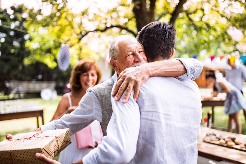 A senior man hugs his son at a family birthday party