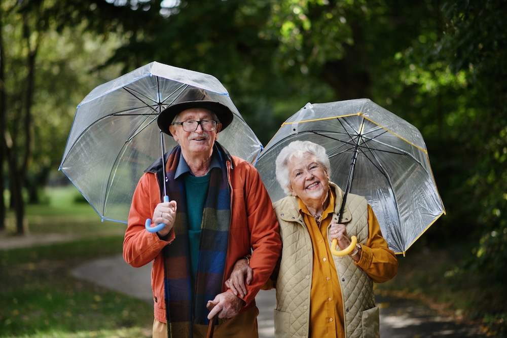 Happy senior couple outside with umbrellas enjoying San Dimas Retirement Communities