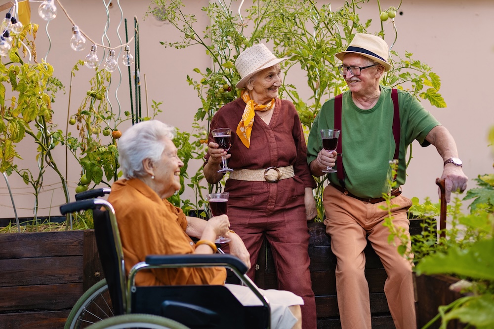 Senior friends spending time in a garden and enjoying wine at their assisted living apartment